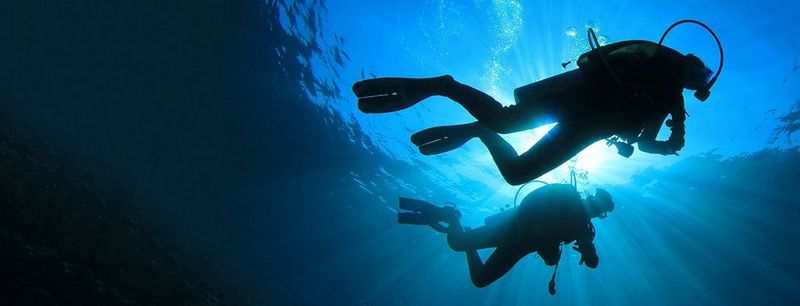 Silhouette of two scuba divers under the sea, lit behind by light from surface of the ocean